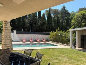 A backyard with a swimming pool, lounge chairs, a table with chairs, and a covered patio area.