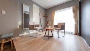 Ein modernes Wohnzimmer mit rundem Tisch, zwei Stühlen, einer Bank, einem großen Fenster mit Vorhängen und einer Deckenleuchte.