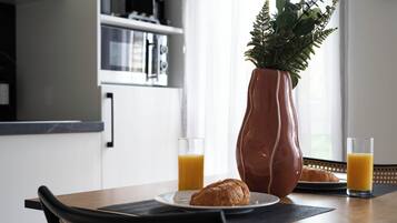 A breakfast table with croissants, a vase with green plants, and glasses of orange juice.
