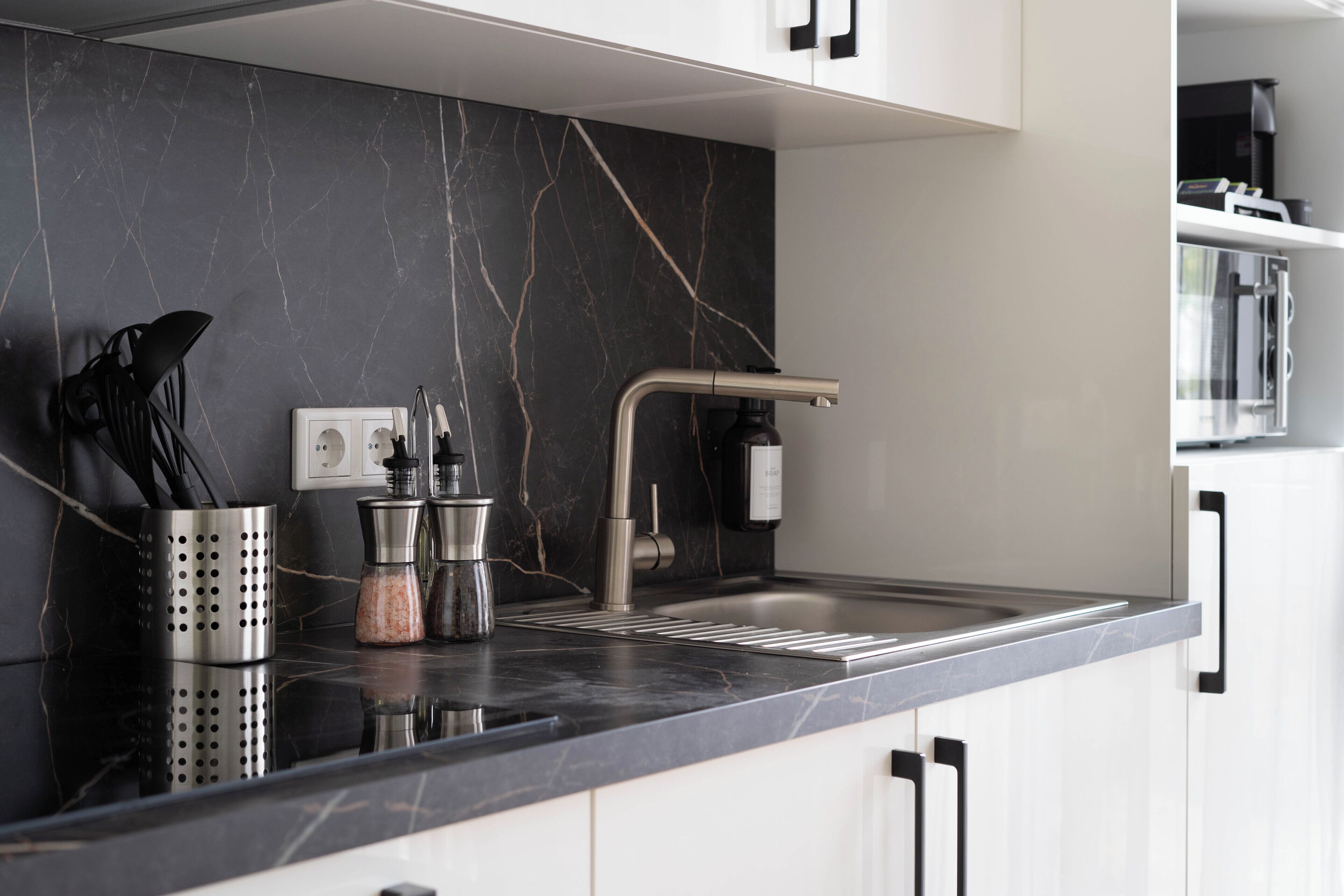 A modern kitchen with a black marble backsplash, stainless steel sink, and white cabinets.