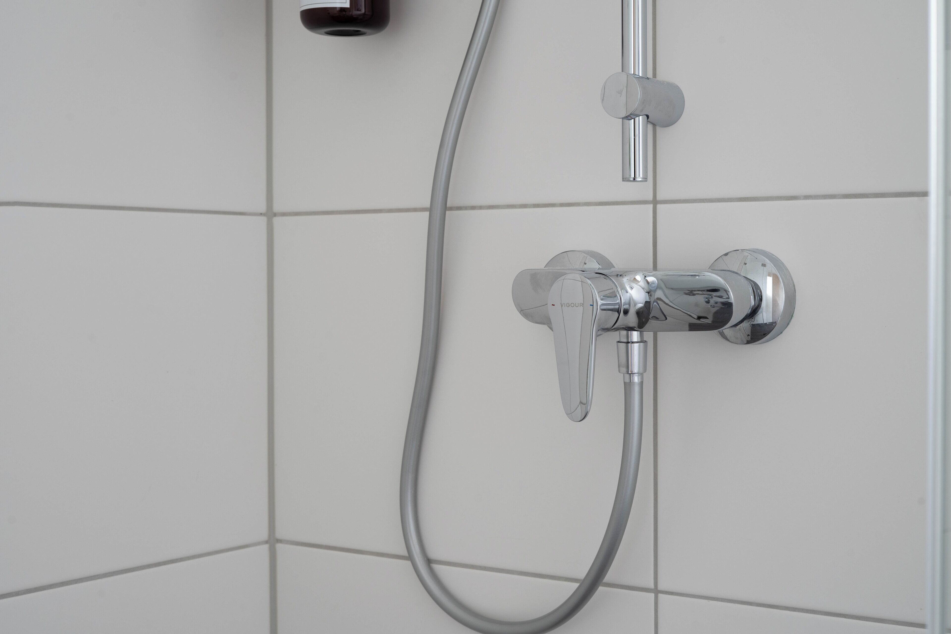 Une douche équipée d’un pommeau de douche à main et d’un robinet mural.