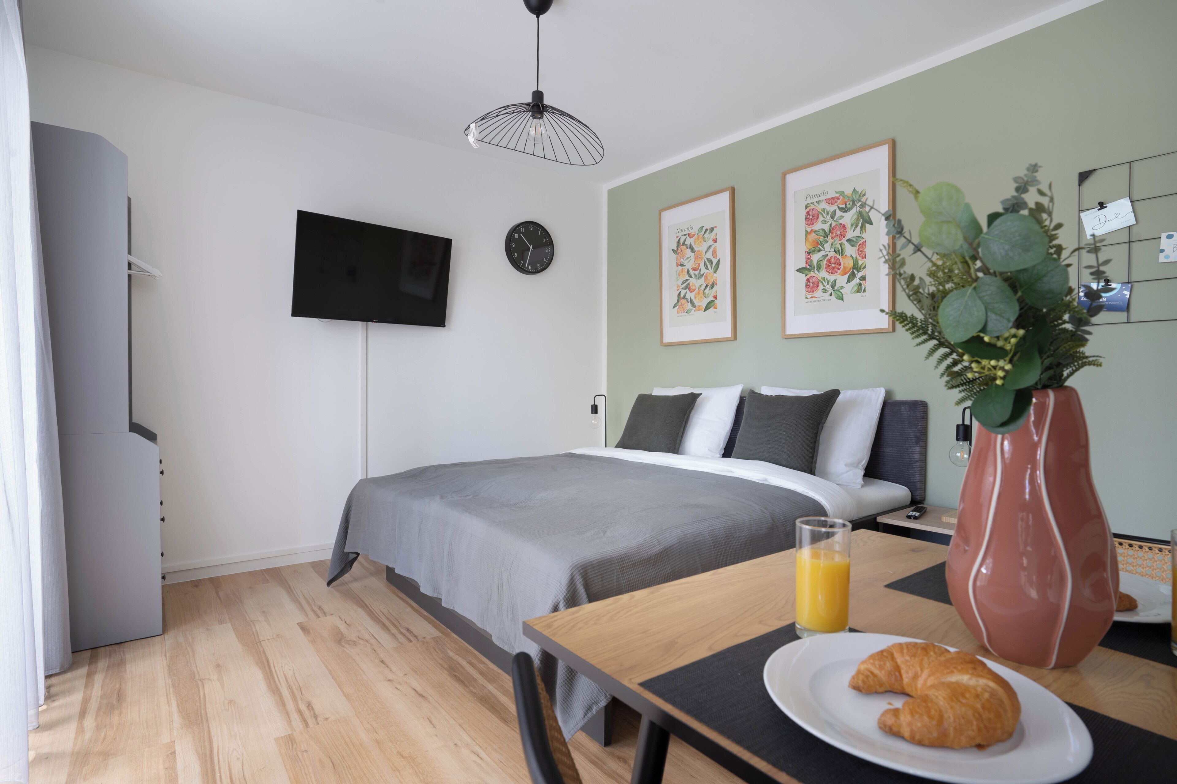 Un dormitorio con cama, mesita de noche y televisor fijado a la pared.