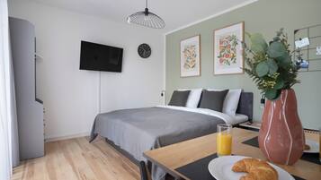 Un dormitorio con cama, mesita de noche y televisor fijado a la pared.