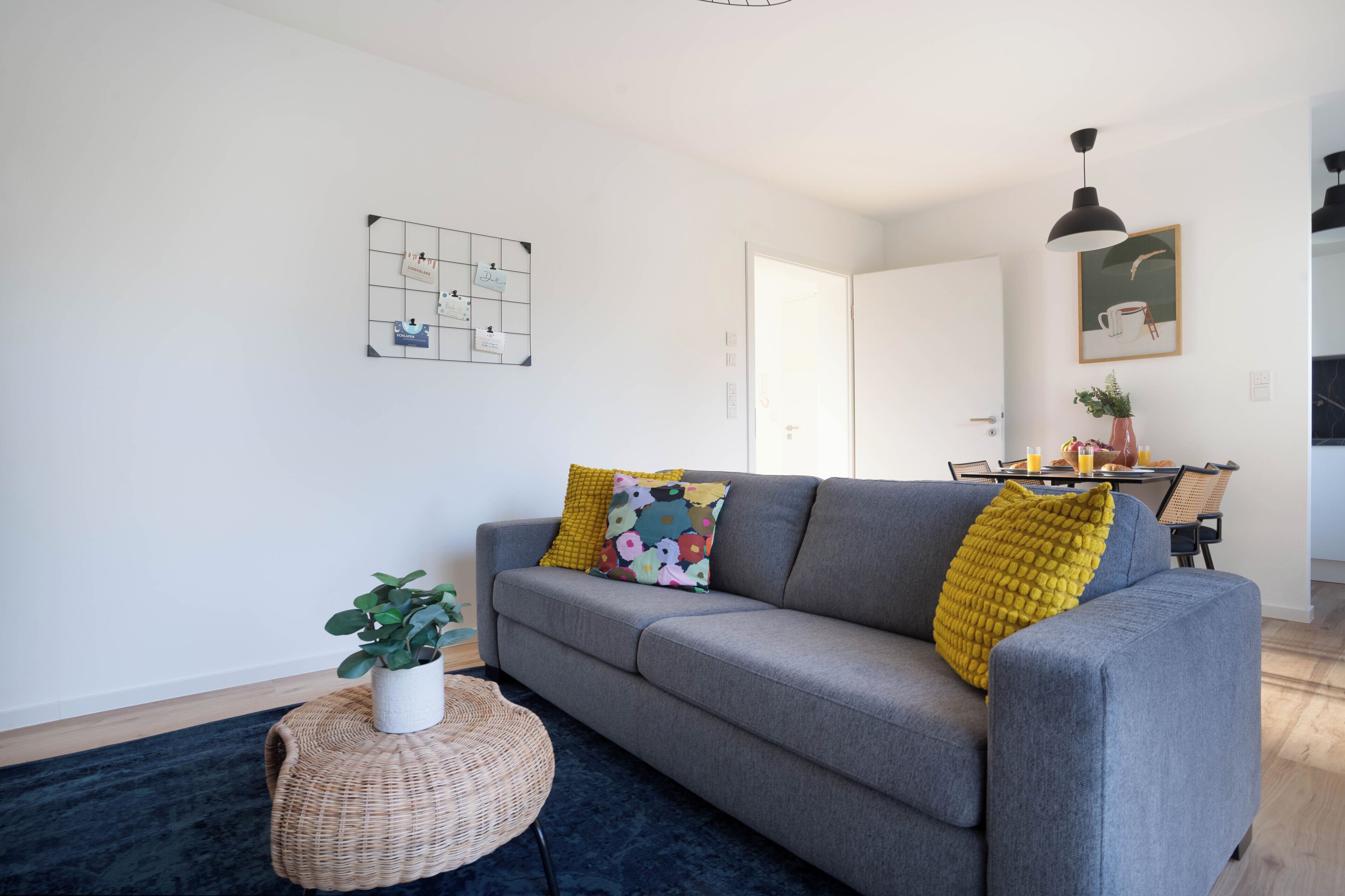 Un salon moderne avec un canapé gris, un pouf rond en osier et un tapis bleu foncé.