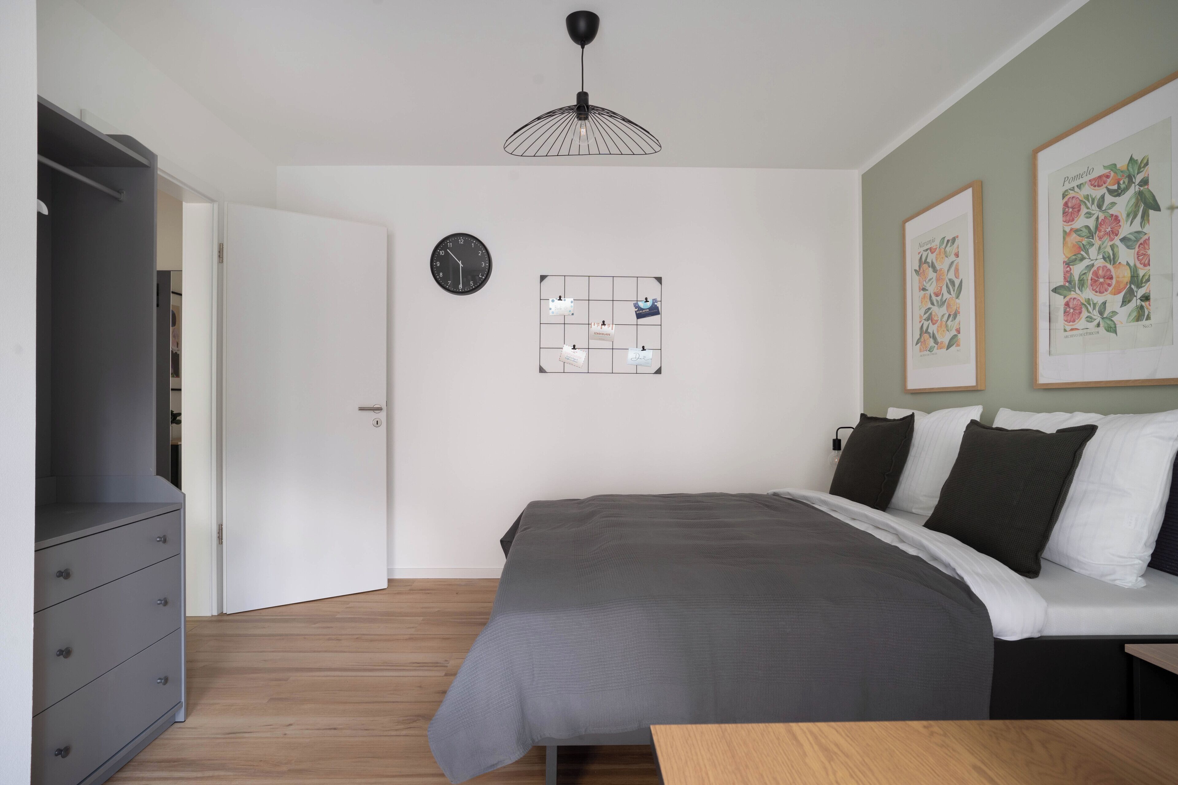 Quarto com cama, penteadeira, relógio e quadros na parede.