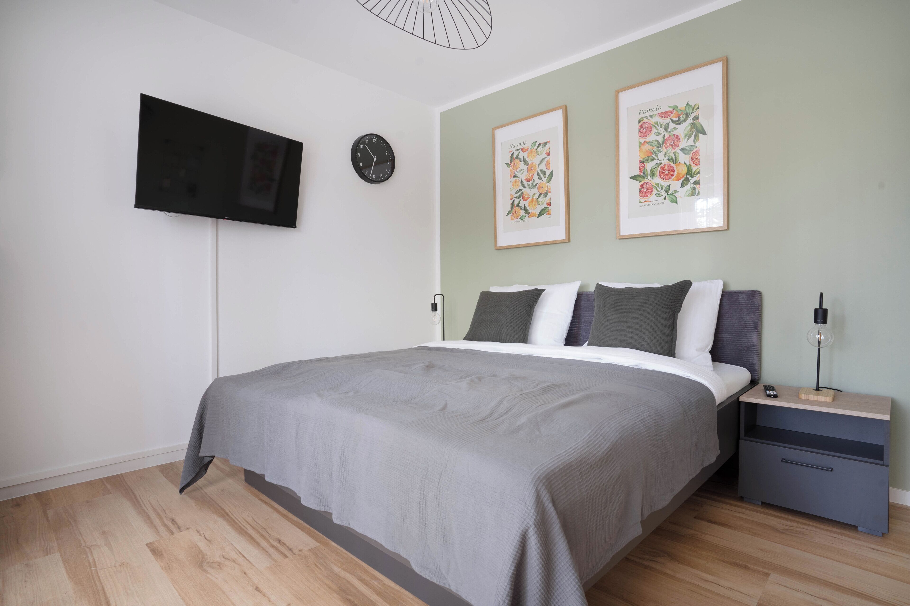 A bedroom with a bed, a nightstand, a TV mounted on the wall, and two framed pictures.