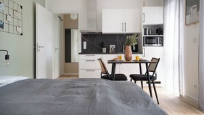 A modern bedroom with a large bed, a dining area with a table and chairs, a kitchen with white cabinets and a black countertop, and a living area with a sofa and a coffee table. - Schöne Apartments in der Innenstadt (Osnabrueck)