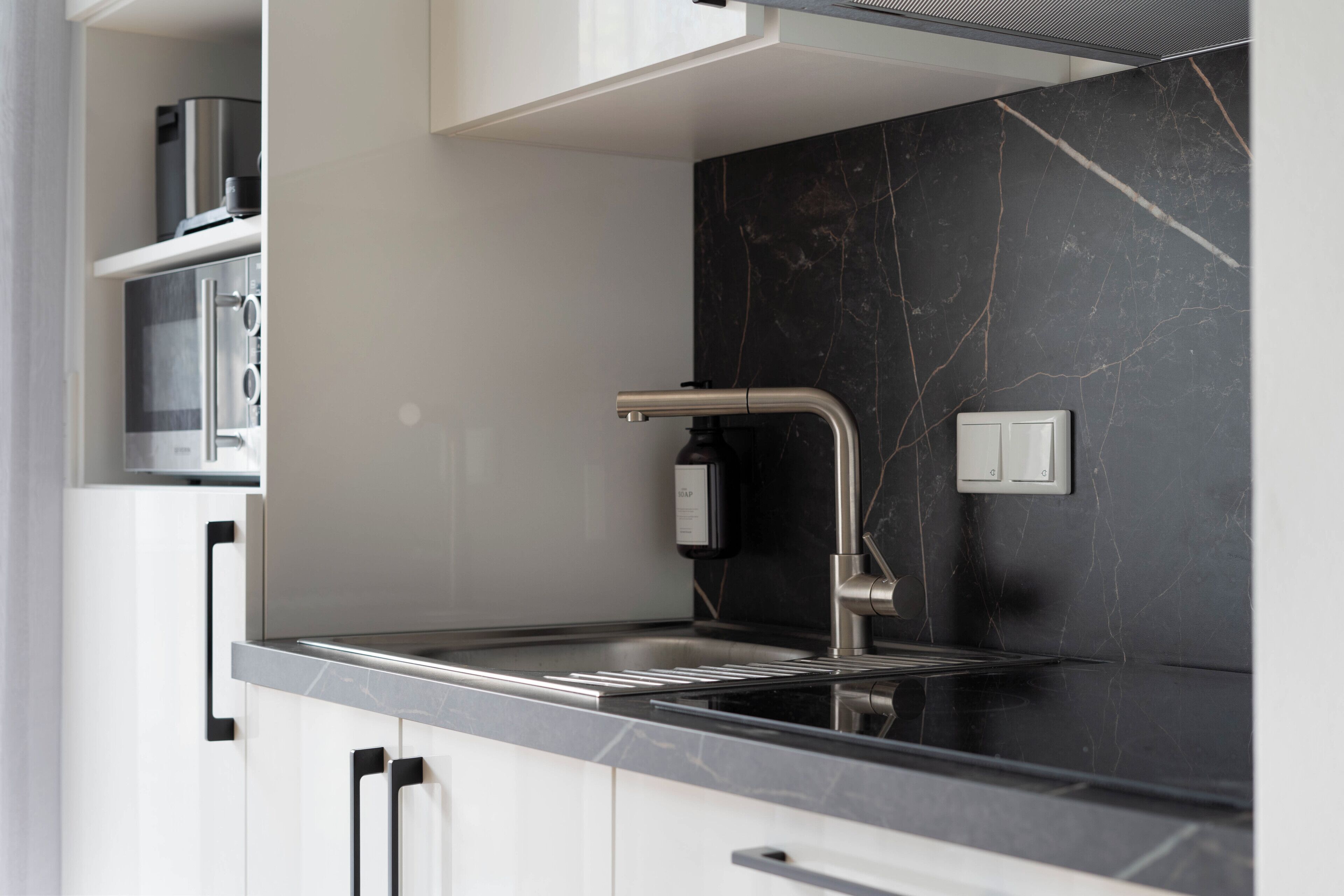 A modern kitchen with a sleek black marble backsplash, stainless steel appliances, and a minimalist faucet.