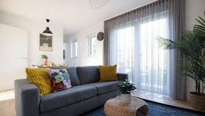 A modern living room with a grey sofa, yellow cushions, a wicker coffee table, and a large window with sheer curtains. - Schöne Apartments in der Innenstadt (Osnabrueck)