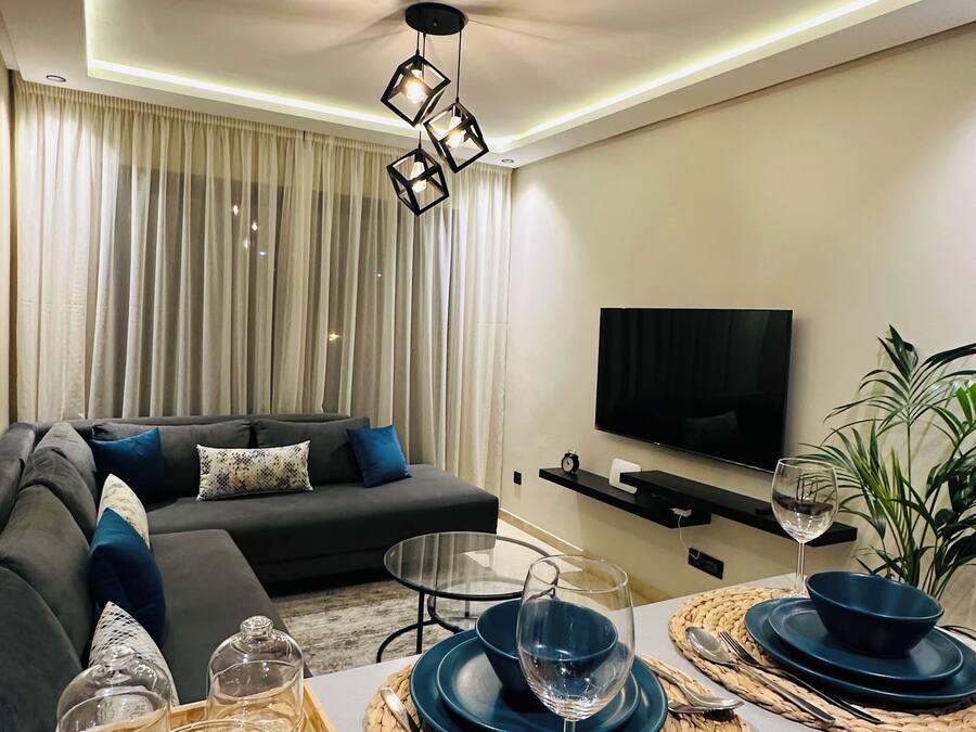 Una sala de estar moderna con un sofá, televisor y un comedor con una bandeja de vasos y platos.