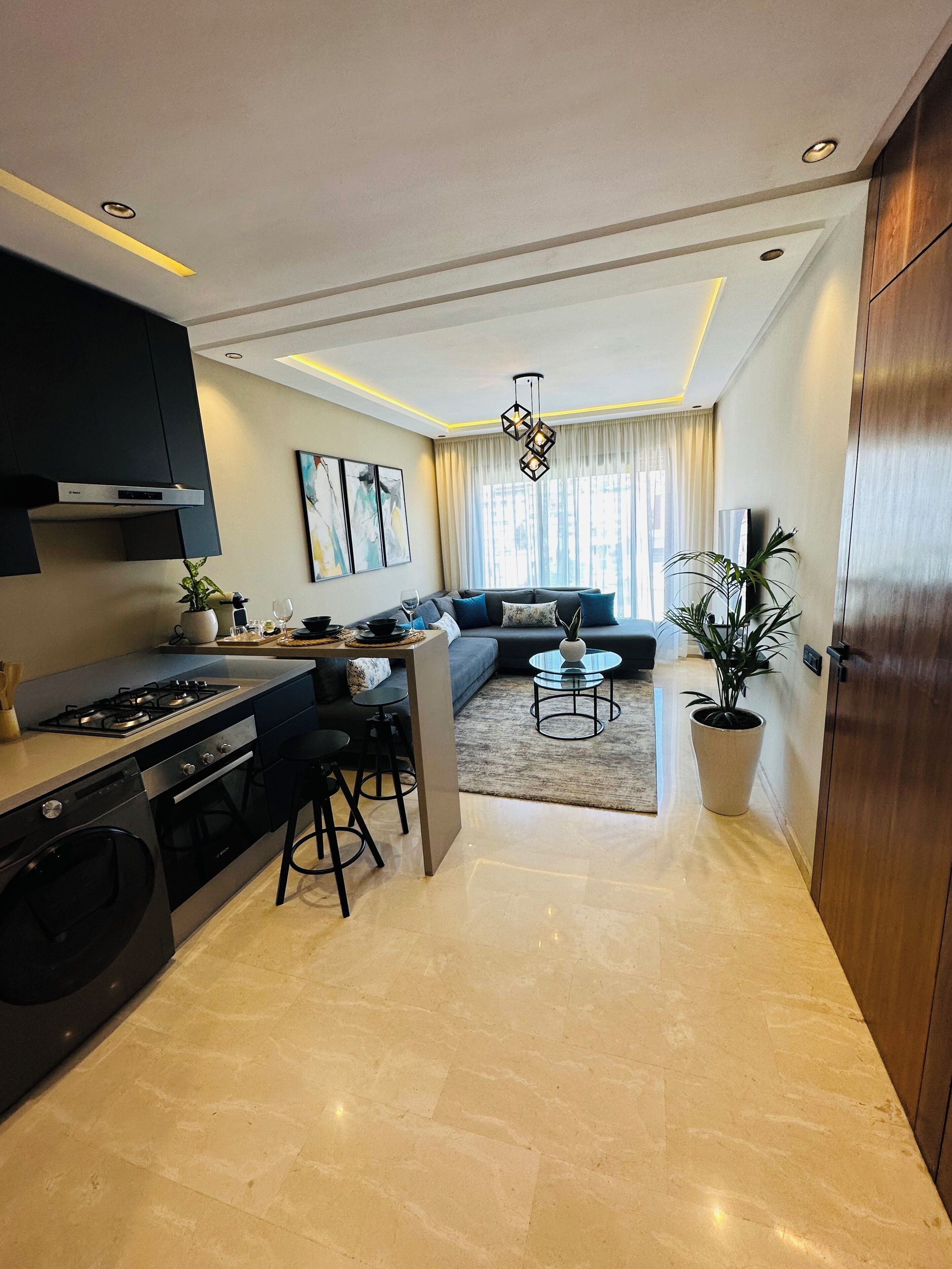 Una cocina moderna con una isla central, un comedor con sofá y una sala de estar con un amplio ventanal.