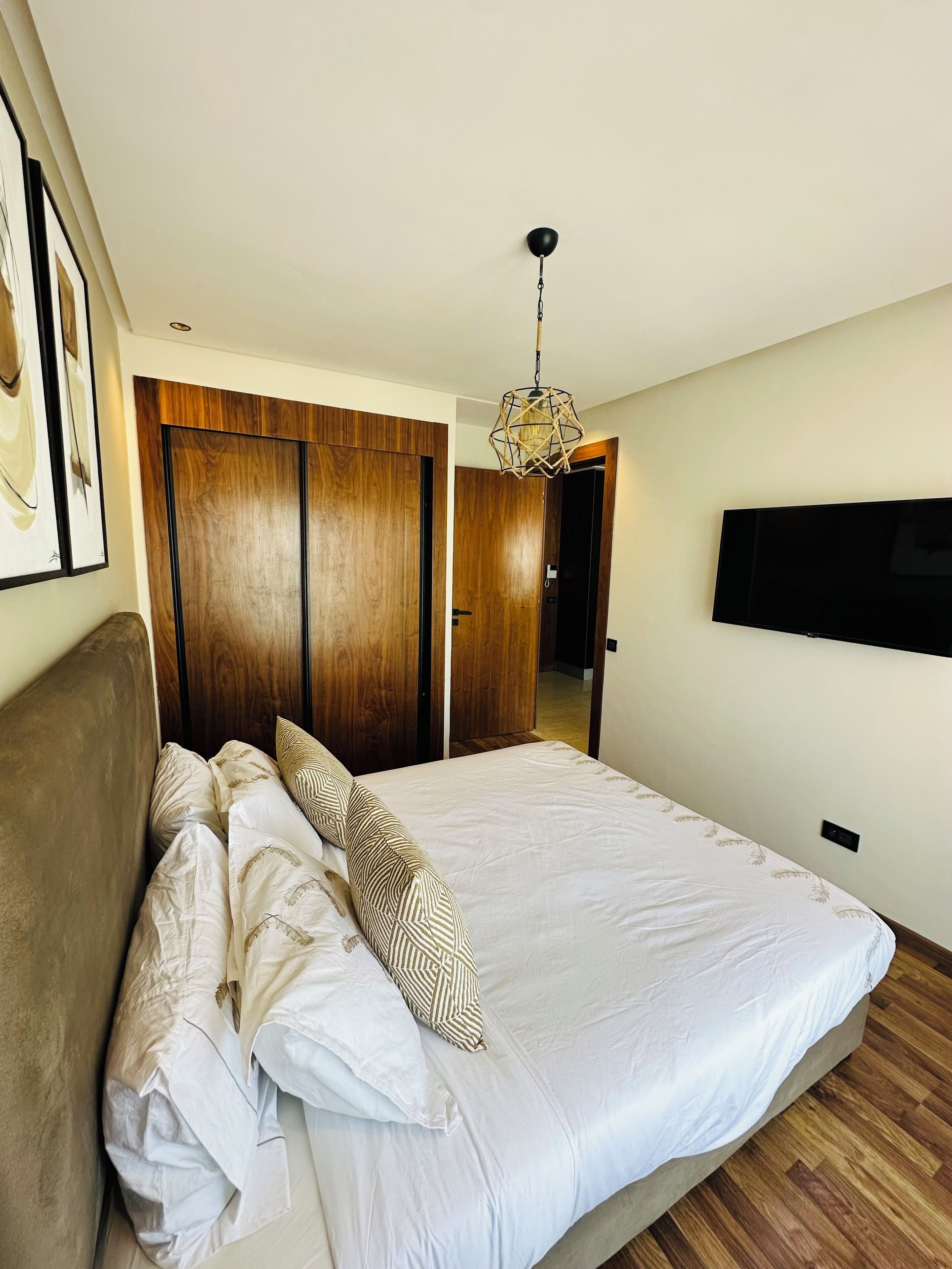 A bedroom with a large bed, wooden wardrobe, and a TV mounted on the wall.