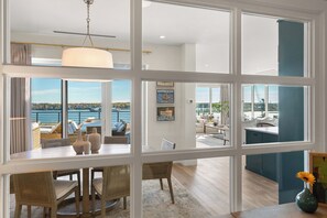 A modern interior with a dining area, kitchen, and living space with large windows overlooking a body of water. - TOP-FLOOR PENTHOUSE at Hobson's Landing.  Sweeping views of Portland's Harbor. (Portland)