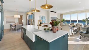 Una cucina moderna con isola centrale, illuminazione a sospensione e vista sul mare.