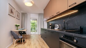 A modern kitchen with a black marble countertop, stainless steel appliances, and a wooden dining area with a chair and table. - Apartamenty Sun & Snow Atal City Square (Wroclaw)