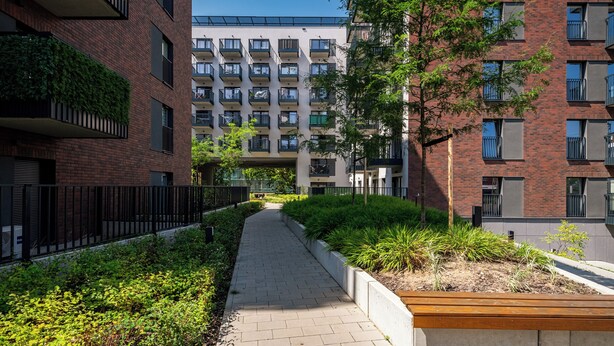 A modern urban apartment complex with a central courtyard, featuring a paved walkway, greenery, and balconies. - Apartamenty Sun & Snow Atal City Square (Wroclaw)