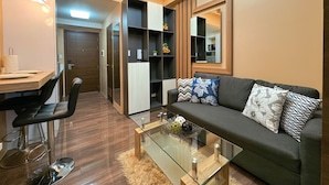 A modern living room with a sofa, coffee table, and a dining area with chairs and a table. - 1BR Makati, Air Residences M005 (Makati)