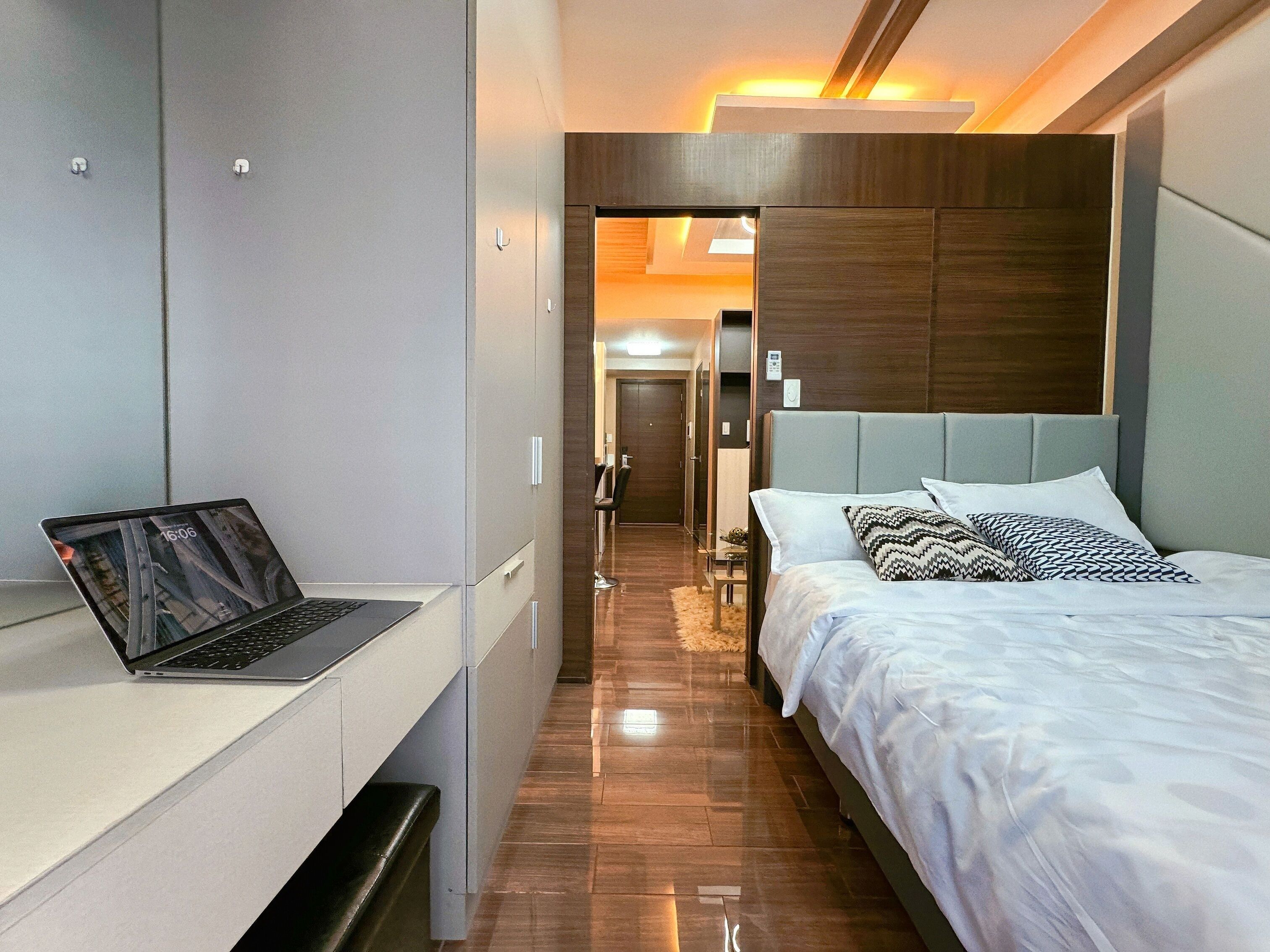 Et moderne hotelværelse med seng, skrivebord med en bærbar computer og et walk-in closet.