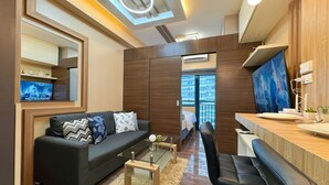 A modern living room with a sofa, coffee table, and a TV on the wall. - 1BR Makati, Air Residences M005 (Makati)