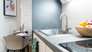 A modern kitchen with a stainless steel sink, a wooden bowl of fruit, and a dining area with a chair and a vase.