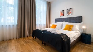 Un lit bien fait, avec des oreillers blancs et orange, une tête de lit sombre et une table de chevet bleue sur laquelle se trouve une lampe.