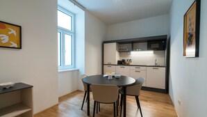 Une cuisine compacte dotée d’appareils électroménagers modernes, un coin repas avec une table ronde et des chaises, et une fenêtre laissant entrer la lumière naturelle.