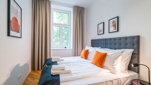 Een moderne slaapkamer met een groot bed, twee kussens, een nachtkastje en een raam met gordijnen.