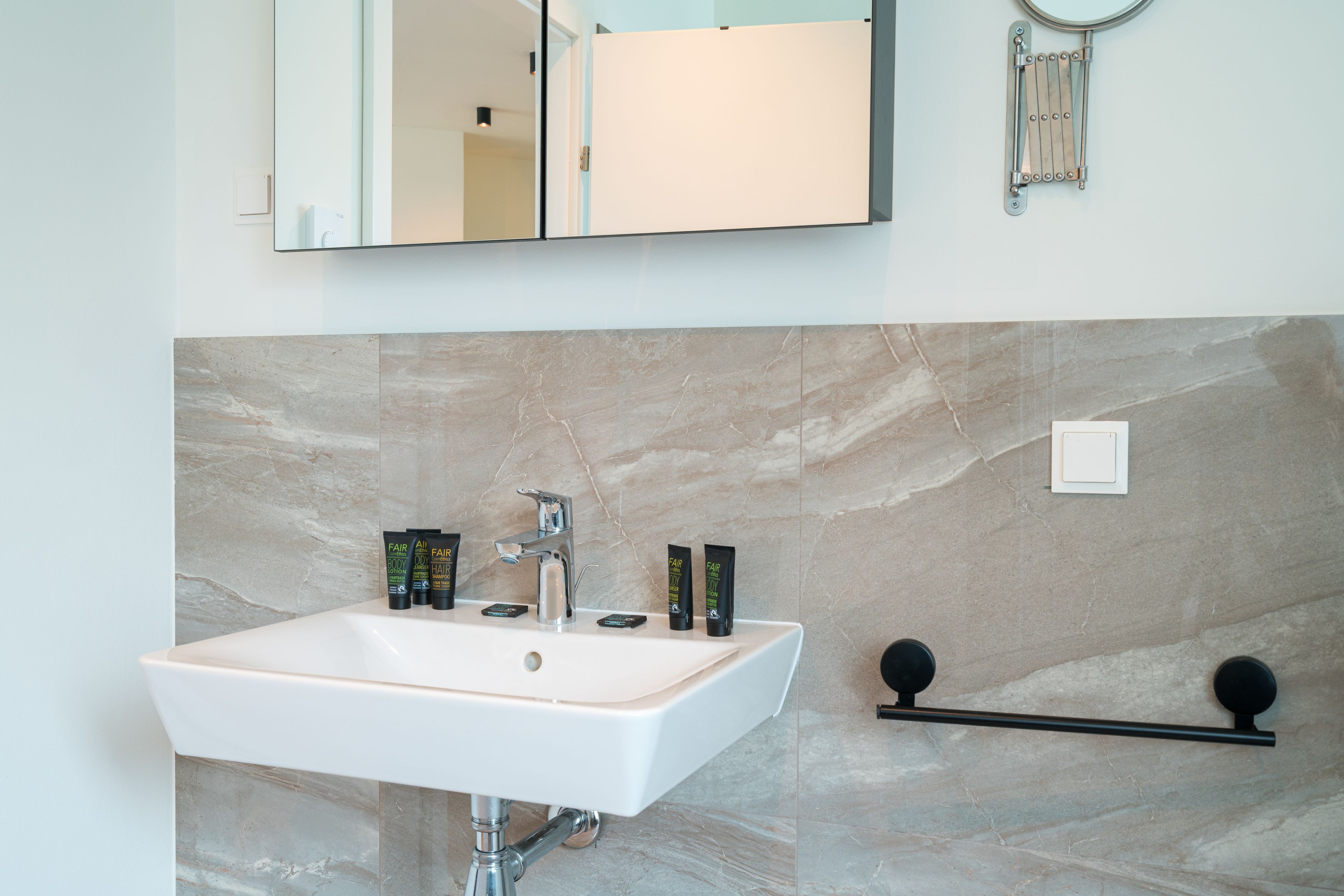 Ett badrum med ett vitt handfat, en spegel och en handdukshängare.