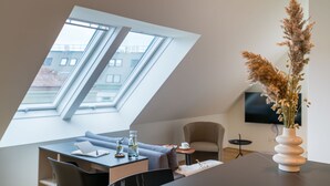 A modern room with a skylight, a dining area, a sofa, a TV mounted on the wall, and a vase with dried plants. - Vienna Residence, Prater - Exhibition Center #6485 (Vienna)