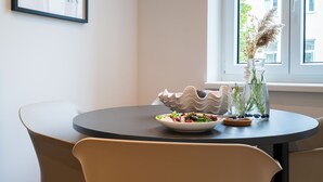 Et spiseområde med et rundt bord, stole, en salatskål, en dekorativ skål og en vase med planter.