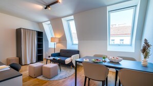 A modern, well-lit room with a sofa, dining table, and ottomans. There are skylights and a large window providing natural light. - Vienna Residence, Prater - Exhibition Center #6460 (Vienna)