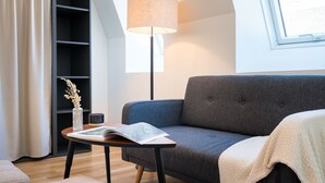 A modern living room with a grey sofa, a small table with a lamp, and a bookshelf. - Vienna Residence, Prater - Exhibition Center #6460 (Vienna)
