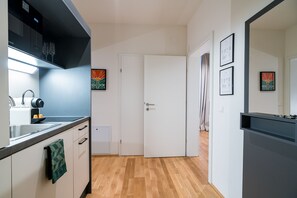 A modern kitchen with a built-in oven, a sink, and a countertop. There is a door leading to another room and a window with curtains. - Vienna Residence, Prater - Exhibition Center #6464 (Vienna)