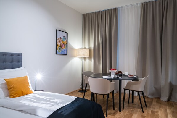 A hotel room with a bed, a desk, chairs, a lamp, and a window with curtains.