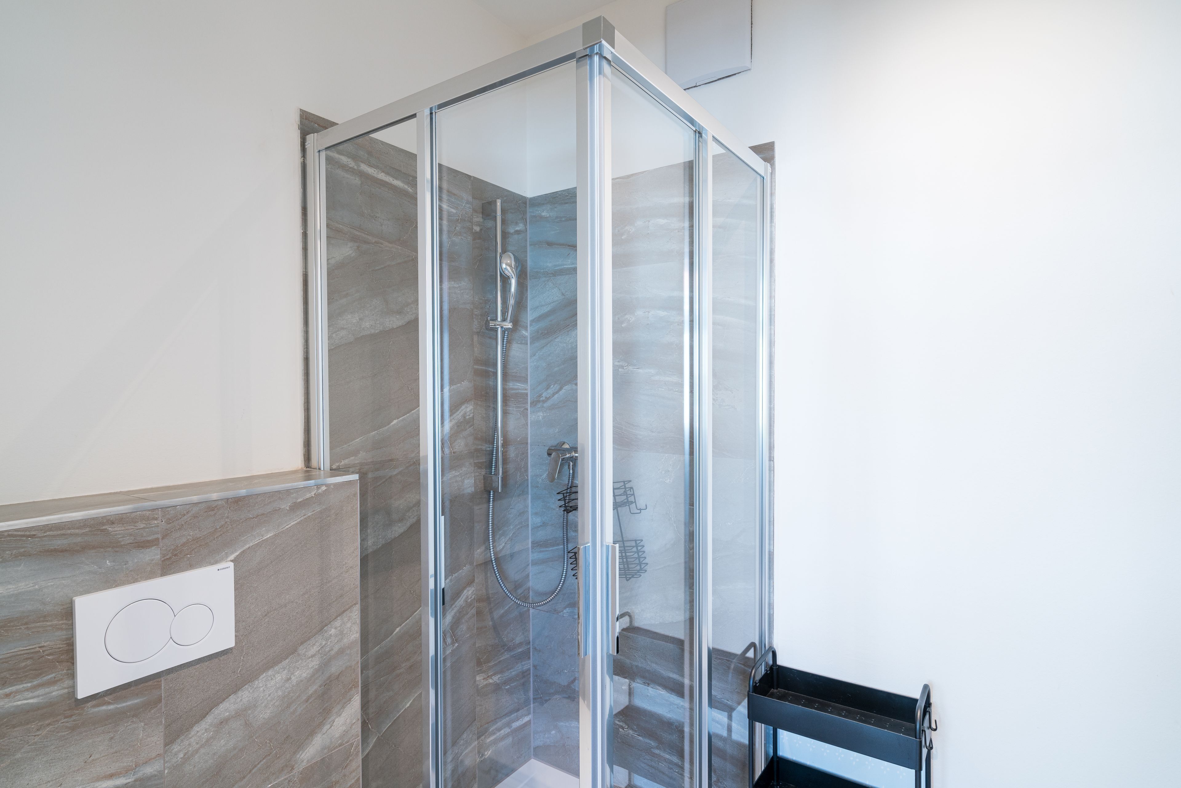 A glass-enclosed shower with a handheld showerhead and a wall-mounted faucet.