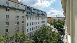 Ein mehrstöckiges Gebäude mit Balkonen, eine Straßenszene und ein klarer Himmel.