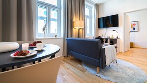 Una habitación de hotel moderna con zona de comedor, sofá, televisor de pantalla plana y escritorio con lámpara.
