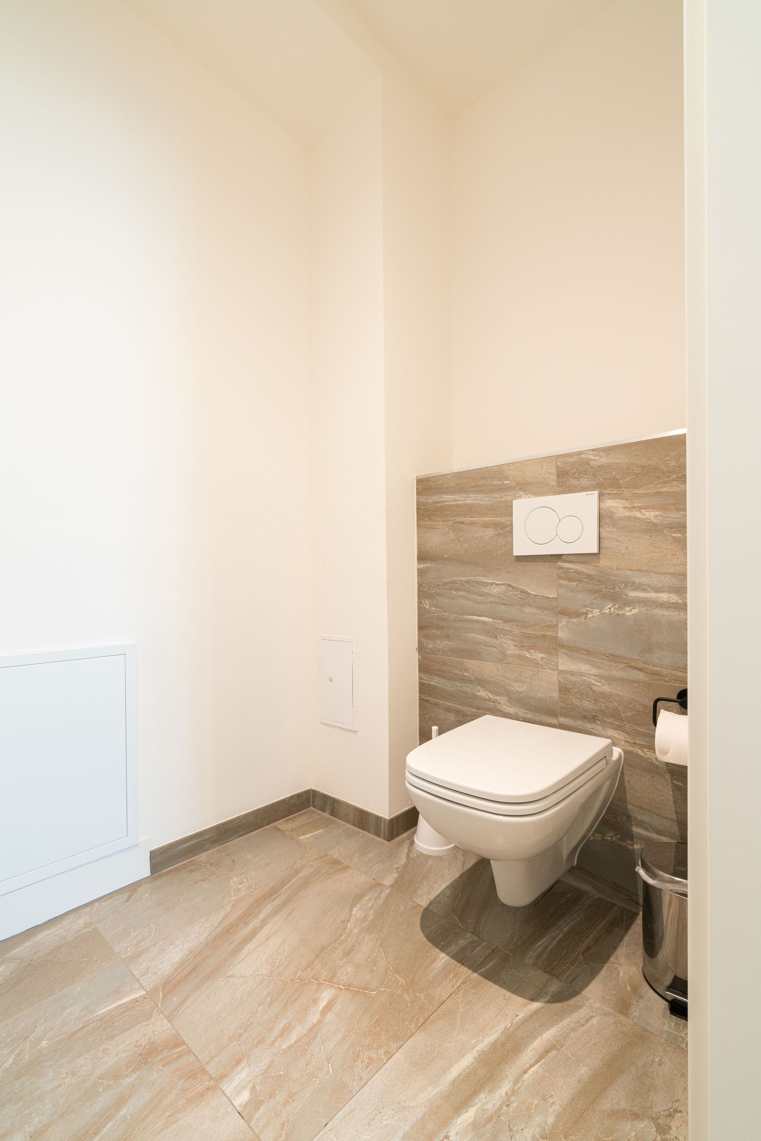 A modern bathroom with a toilet, a wall-mounted sink, and a trash can.