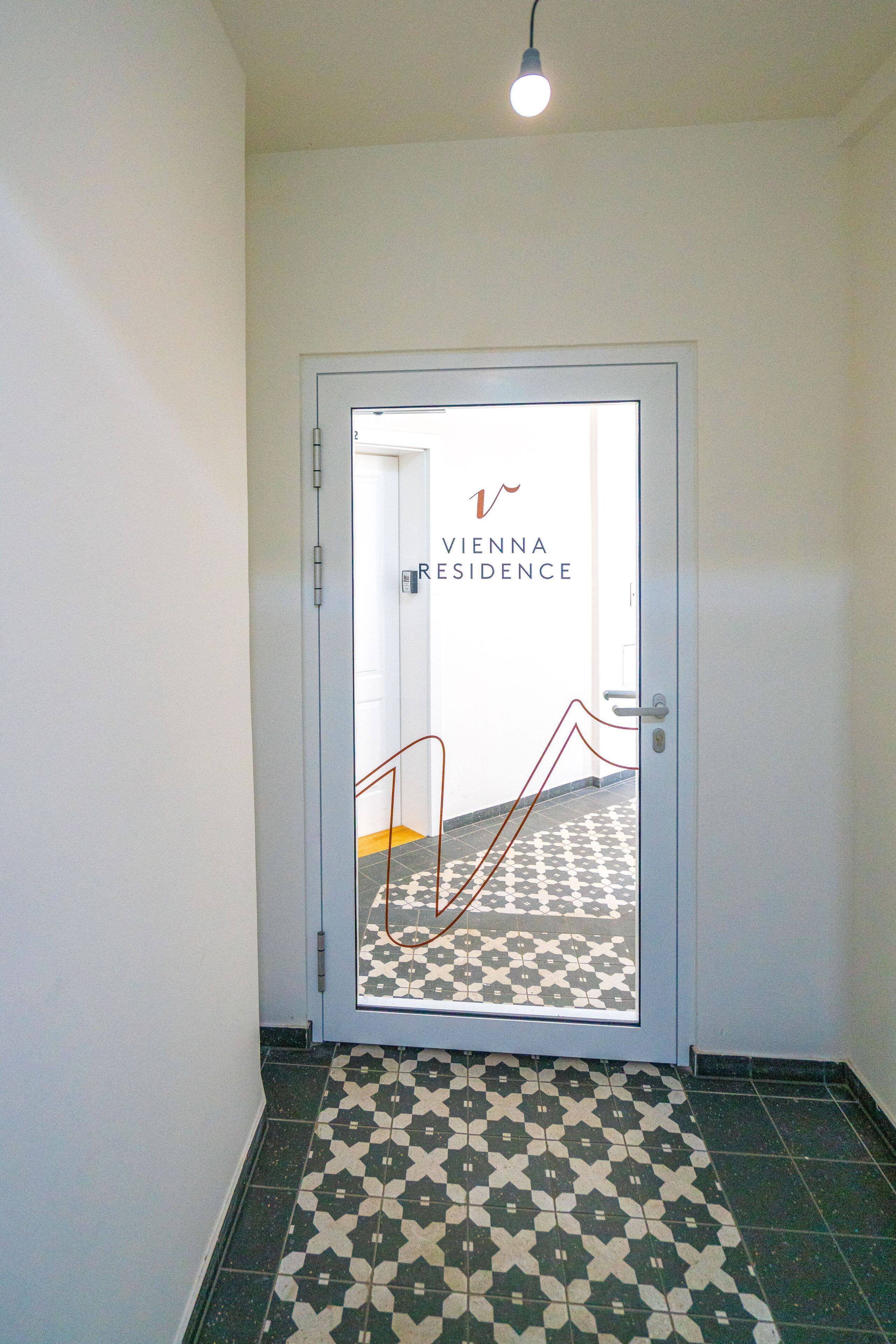 Un couloir au sol décoré d’un motif menant à une porte portant l’inscription « Résidence de Vienne ».