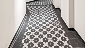 Un couloir aux murs blancs, dont le sol est recouvert de carreaux noirs et blancs formant un motif, et une porte se trouve au bout.