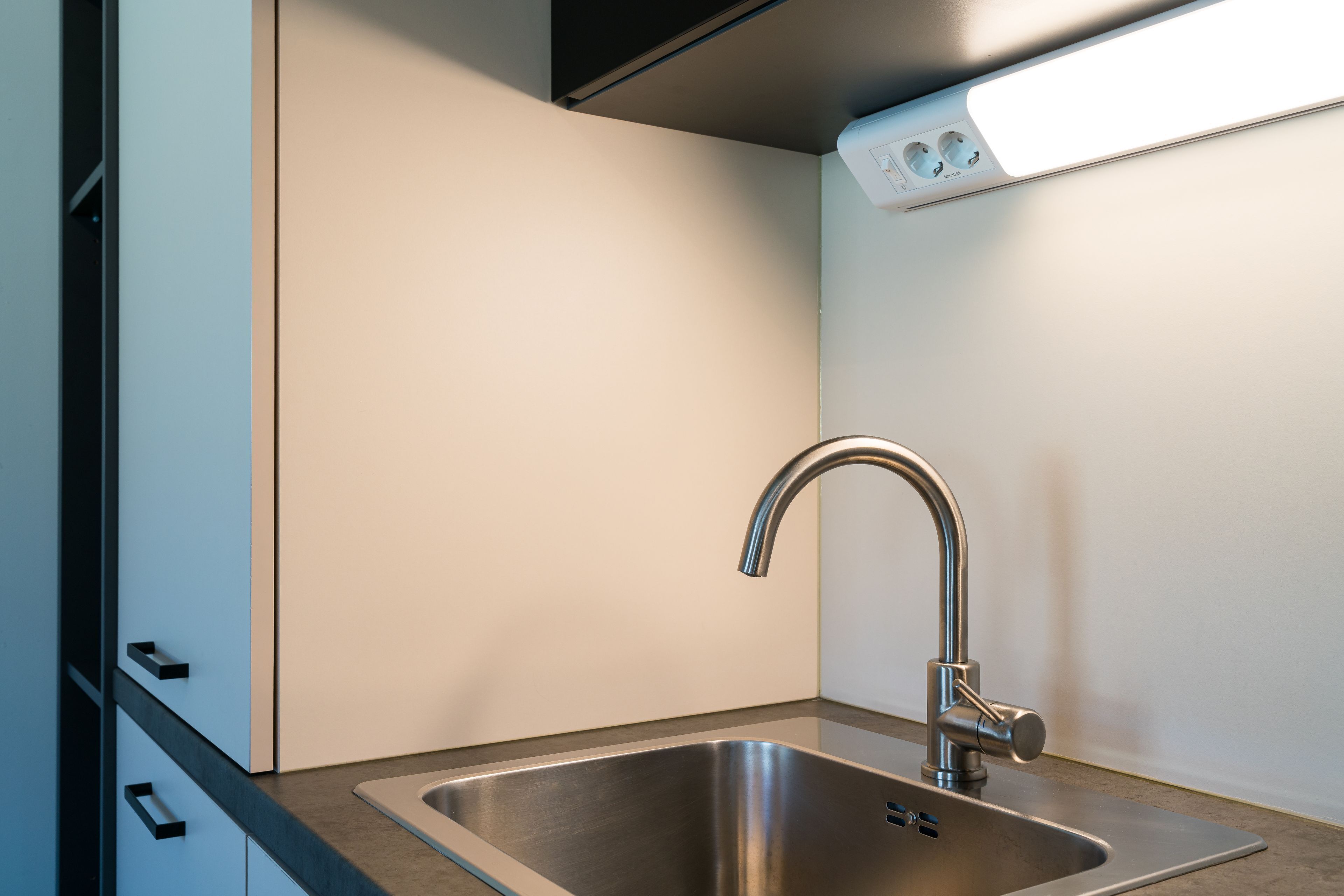 Een moderne keuken met een roestvrijstalen spoelbak, een strakke kraan en een inbouwlamp boven de spoelbak.