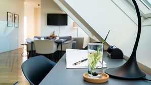 Un coin repas moderne avec une table, des chaises, un verre d’eau garni d’une tranche de citron et d’une branche de romarin, un carnet et une lampe.