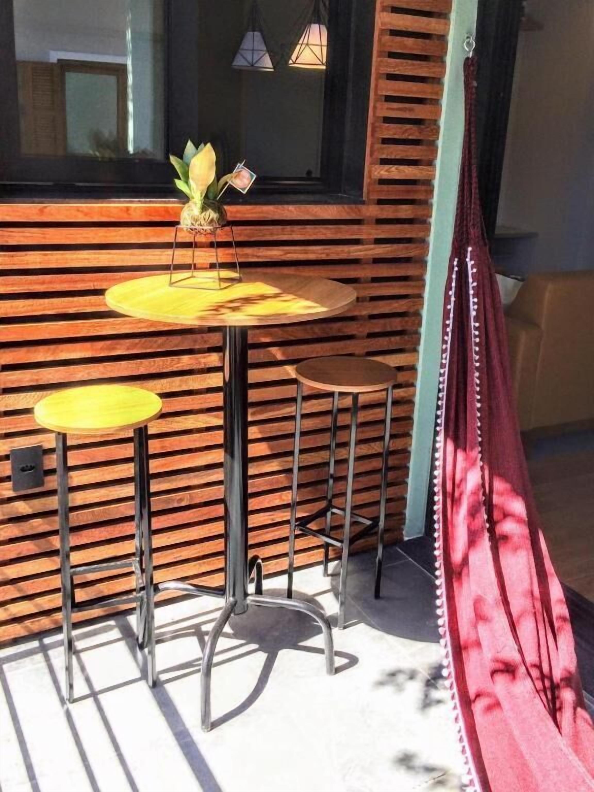 A cozy outdoor seating area with a wooden slatted wall, a round yellow table, and a red hammock.