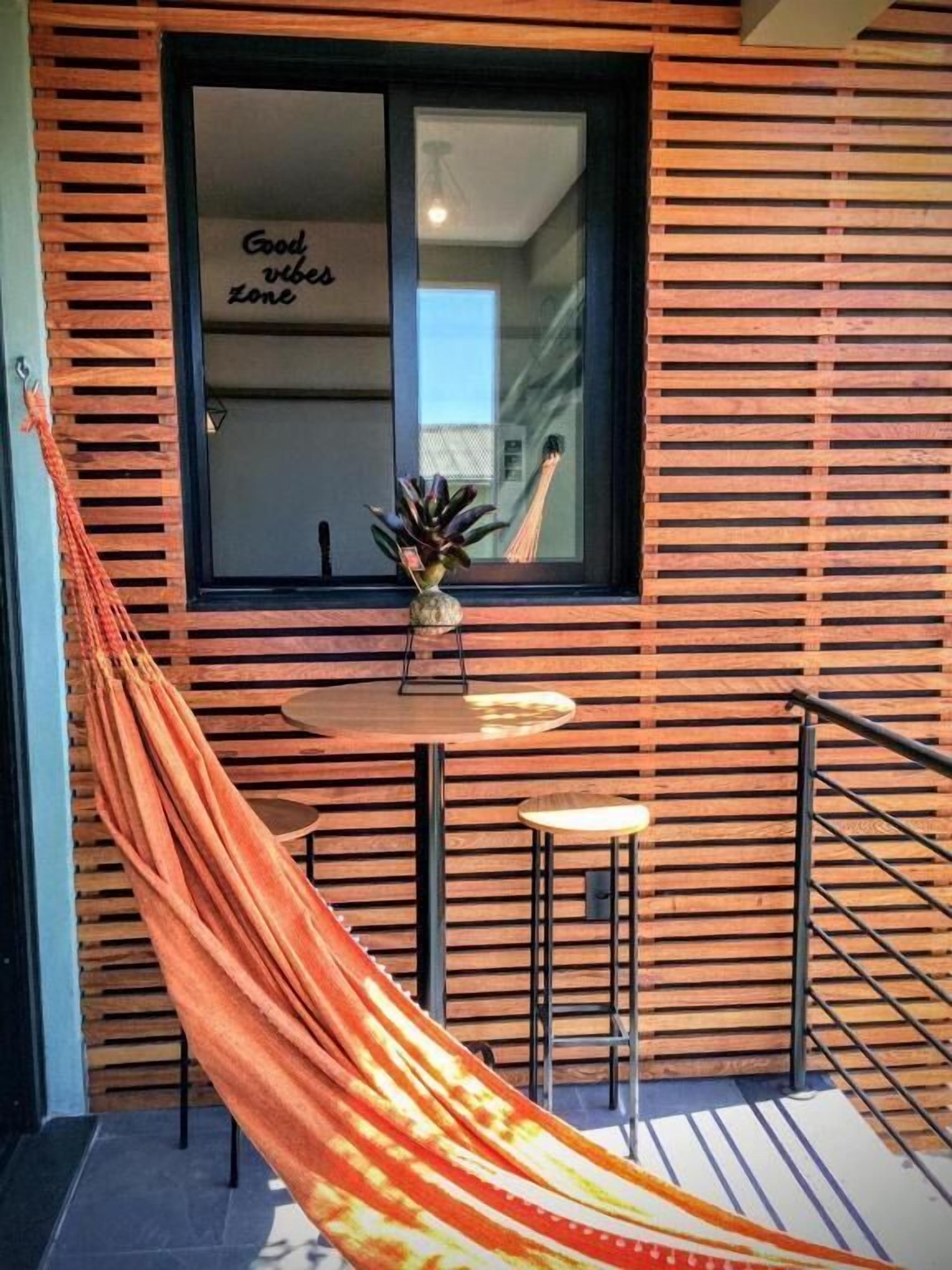 A hammock in a room with a window, a small table, and a chair.