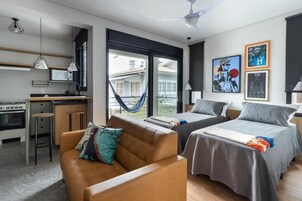 Una camera d'albergo moderna con angolo cottura, due letti, una poltrona e ampie finestre.