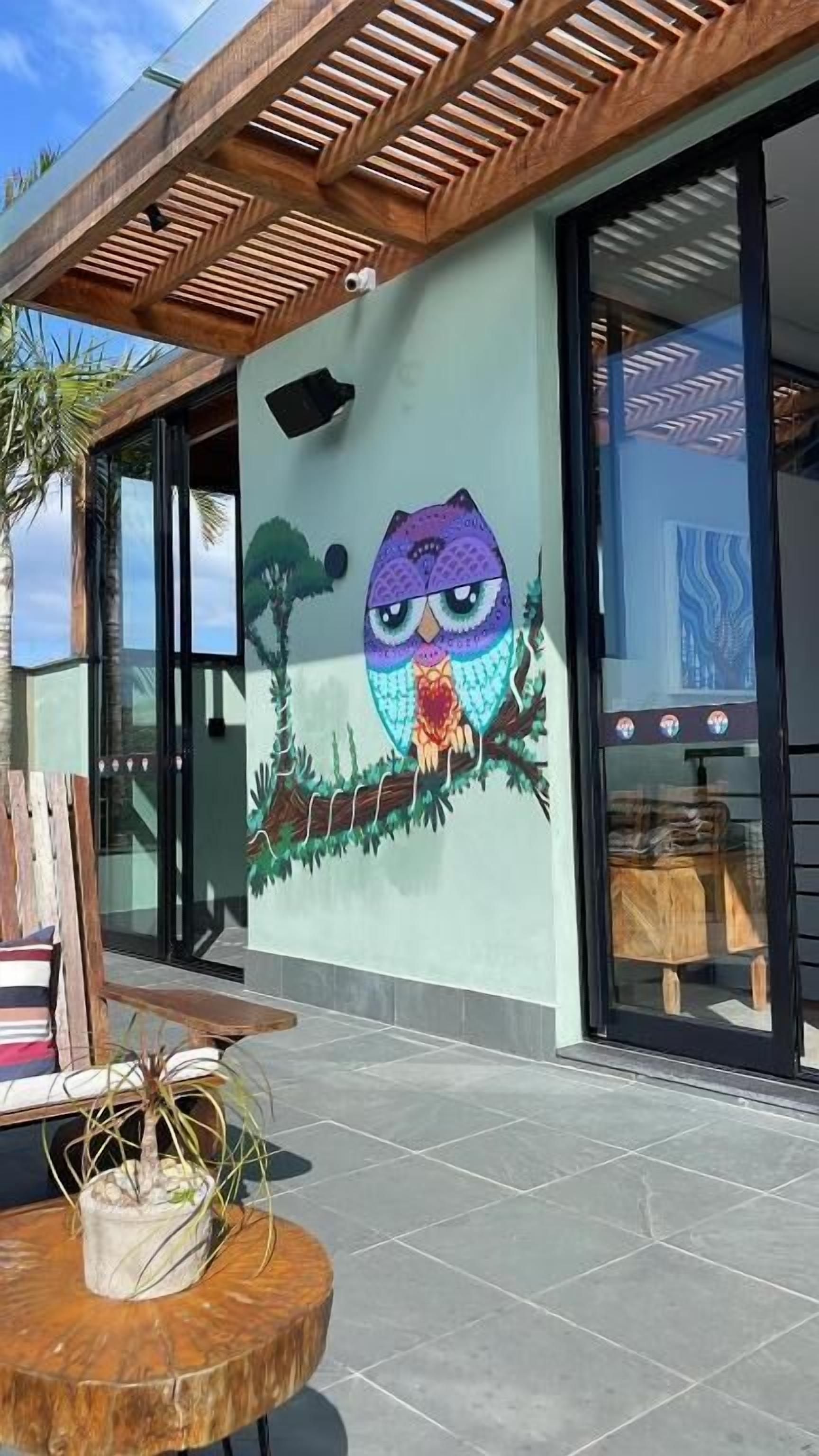 A building exterior with a large mural of an owl, a wooden pergola, and a glass door.