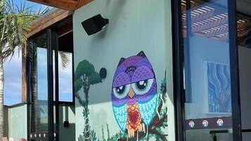 A building exterior with a large mural of an owl, a wooden pergola, and a glass door.