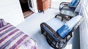 Une pièce avec un plafond en bois, un lit recouvert d’une couvre-lit à motifs, une chaise en osier avec un coussin bleu et une commode en bois.