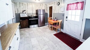 Une cuisine compacte équipée d’un réfrigérateur, d’un four à micro-ondes et d’une cuisinière. On y trouve une table à manger avec des chaises, ainsi qu’un tapis rouge près de la porte.