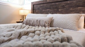 A bed with a textured blanket and pillows, a wooden headboard, and a bedside lamp. - Stylish Escape/Game Room/4 Brs (Arlington Heights)